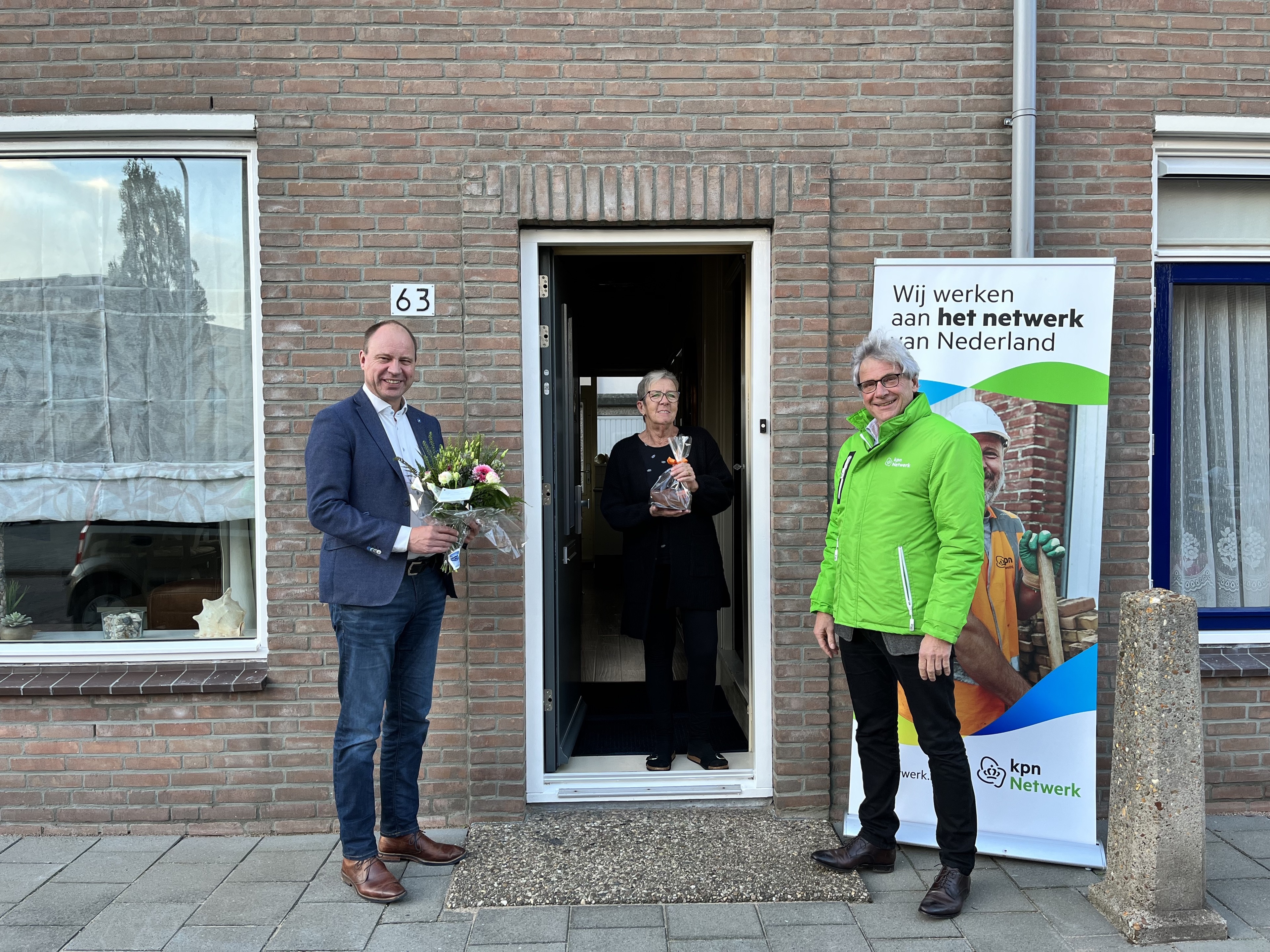 Wethouder Bram Diepstraten (l) en Frans Dankaart van KPN zetten mevrouw Beijdorff in de bloemen. Zij werd als eerste in IJmuiden op het glasvezelnetwerk aangesloten.
